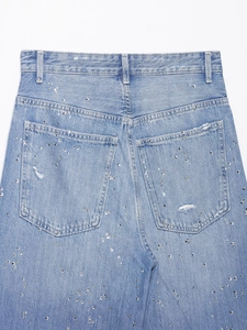 Détails du pantalon en jean bleu clair orné de strass brillants et de finitions usées