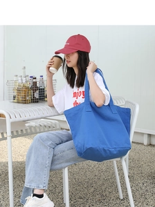 Lifestyle shot of a woman carrying a large blue washed canvas tote bag in a bright cafe