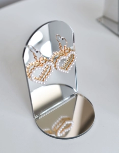 Macro view of heart-shaped pearl drop earrings on a small arched mirror display