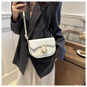 White faux leather saddle bag with golden ring clasp shown on model in cozy home setting