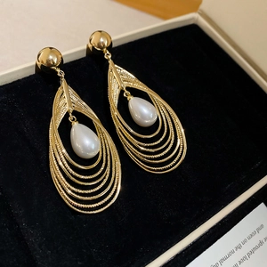 Detailaufnahme mehrlagiger goldener Ohrringe mit Tropfenperle auf Samt