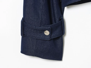Close-up of deep blue denim jacket sleeve with adjustable silver metal button closure