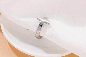 Detailed close-up of a silver polished stainless steel cross ring on white fabric