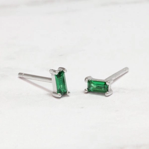 Detailed view of rectangular emerald stud earrings with silver prongs on white marble