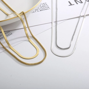 Layered gold and silver snake bone chain necklaces on white minimalist background