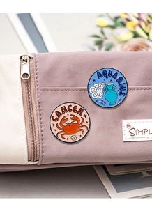 Detail showing Cancer and Aquarius enamel pins on a light purple fabric bag
