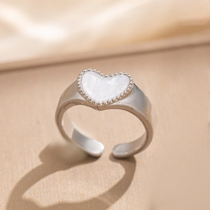 Detail view of silver heart shell ring with beaded edge on minimalist beige texture