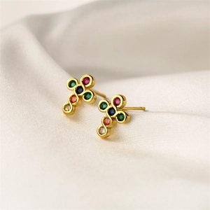 Detailed macro shot of gold-plated cross earrings with colorful gemstone inlays on silk