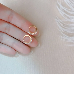 Macro view of gold pearl hoop earrings held on finger showing small dainty design