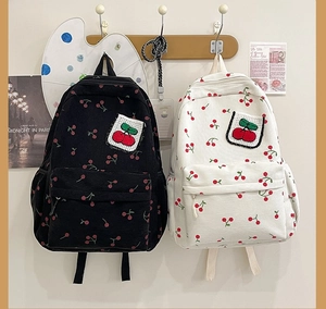 Zaini carini in velluto a coste nero e beige con ricamo a ciliegia appesi a un gancio