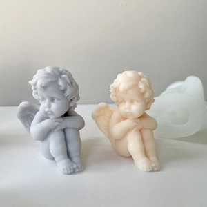 Detailed view of two small angel wax ornaments in grey and cream next to a silicone mold
