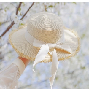 Detail of handwoven straw hat featuring white bow ribbon and frayed brim edges