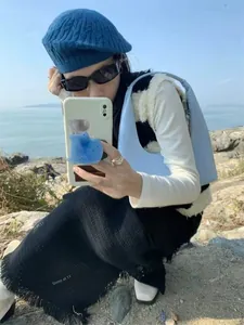 Outdoor shot of a light blue crescent shoulder bag paired with a blue cable knit beret