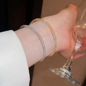 Gros plan de bracelets en maille de zircon or et argent portés avec un verre à vin