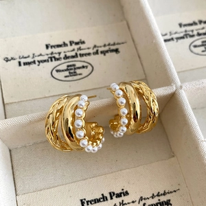 Detail of gold multi-layer C-shaped earrings with wire wrap and white pearls in a jewelry box