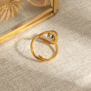Detail of gold-tone stainless steel open ring featuring a sphere ornament on textured fabric