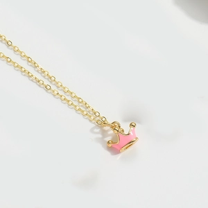 Close-up of gold chain necklace featuring a pink enamel crown pendant on white background