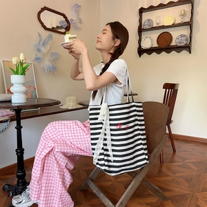 Detail of striped canvas tote bag with lace bow and red embroidery in a vintage cafe