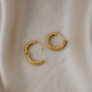 Detailed macro of gold striped hoop earrings on champagne silk showing the hinge clasp