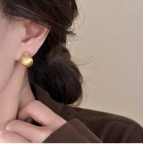 Close-up of matte 18k gold plated teardrop earring worn by a model in natural light