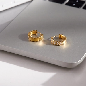 Vue rapprochée de boucles d'oreilles créoles dorées en acier avec texture vague