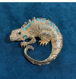 Macro detail of golden lizard brooch with blue rhinestones on a teal velvet surface