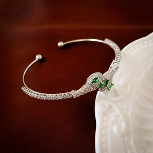 Detail shot of a silver snake-shaped cuff bracelet with green gemstones on a white ceramic plate