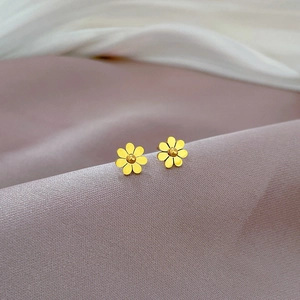 Detail shot of golden floral titanium steel stud earrings on soft textured fabric