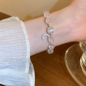 Detailed shot of a pale pink beaded bracelet with opal bead and silver crescent moon charm