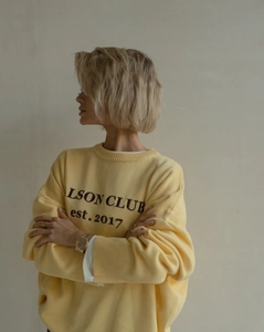 Detail view of bright yellow knit sweater with LSON CLUB lettering and rib texture