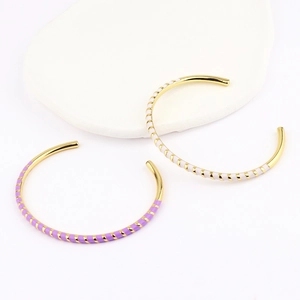 Close-up of gold enamel C-shaped open bangles with purple and white stripes on stone