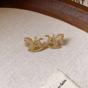 Macro detail of gold horse earrings with crystal pavé on a rustic wooden tray