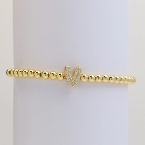 Elastic gold bead bracelet with crystal-paved bubble letter V pendant on white stand