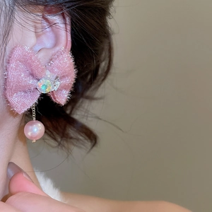 Close-up of pink fabric bow earring with crystal and pearl drop worn by model