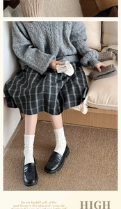 Close-up of white cable knit socks paired with black loafers and a plaid skirt