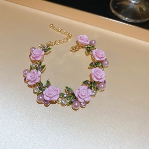Detail of floral bracelet featuring pink roses, green leaves and pearls with golden chain