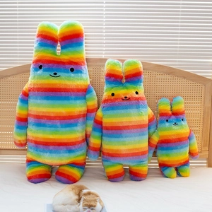 Rainbow striped rabbit plush toys in three sizes on a cozy white bed with natural light