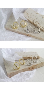 Detailed close-up of gold and silver irregular geometric earrings on a beige stone base
