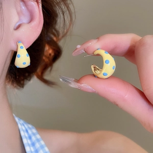 Detail of C-shaped yellow earrings with blue polka dots worn by a model
