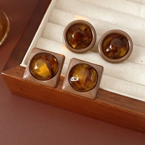 Macro detail of amber-colored geometric round and square stud earrings in a wooden box