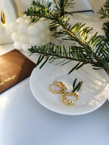 Close-up of golden twisted hoop earrings on a ceramic tray with lifestyle props