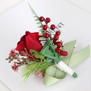 Artificial red rose boutonniere with berries, green leaves, and ribbon for weddings