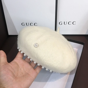 Close-up of a cream wool beret featuring pearl trim and a metallic silver M logo badge