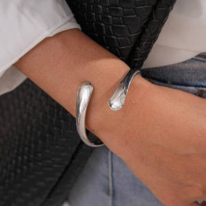 Close-up of a silver irregular oval cuff bangle featuring teardrop ends on a model's wrist