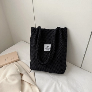 Fashionable black corduroy tote bag for women featuring a white logo patch on a minimalist desk