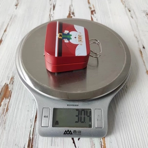 Detailed view of a Christmas tin candy box with Santa pattern on a scale weighing 30.4g