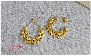 Détail de boucles d'oreilles créoles dorées 18K en forme d'épi sur fond gris