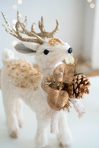 Detail of white reindeer figurine with gold glitter antlers and decorative pine cone