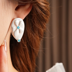 Detail of vintage silver teardrop earring with flower relief and turquoise stones on ear