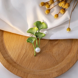 Detailed macro view of green ginkgo leaf brooch with pearls on wooden tray